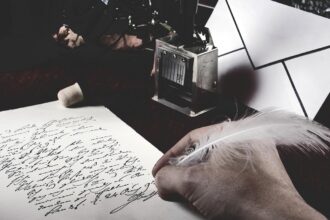 Un hombre escribe con una pluma junto a un tintero una caligrafía clásica.