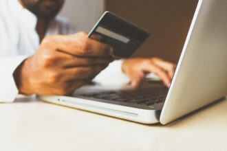 Un hombre mira una tarjeta de credito mientras teclea en el ordenador