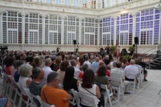 Numeroso público sentado en sillas blancas en el Patio del Palacio de la Diputación escuchando una agrupación musical que tienen delante.