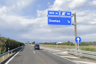 Carretera con dos carriles de circulación, con cartel azul que indica que la salida 96 en dirección a Dueñas está a 500 metros y con una furgoneta circulando por el carril derecho.