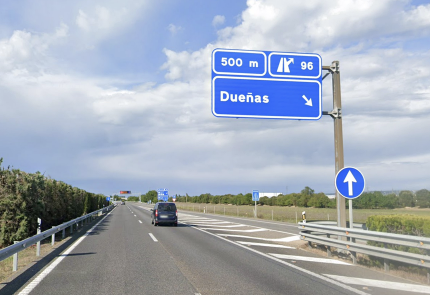 Carretera con dos carriles de circulación, con cartel azul que indica que la salida 96 en dirección a Dueñas está a 500 metros y con una furgoneta circulando por el carril derecho.