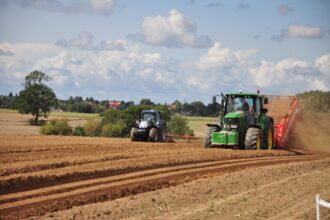 Un tractor verde y otro azul aran una parcela de cultivo de forma parelela.