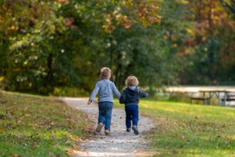 Un par de niños corren dados de la mano por una senda de un parque