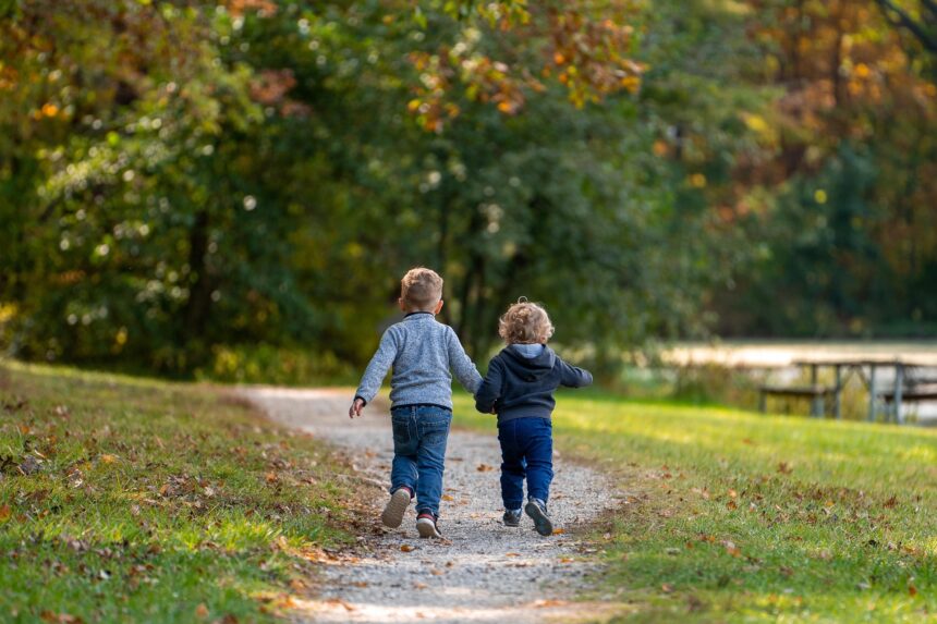 Un par de niños corren dados de la mano por una senda de un parque