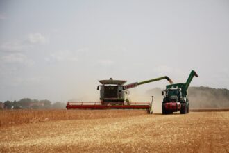 Una cosechadora avanza junto a un tractor con carro recogiendo la cosecha