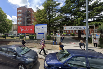 Carteles de la constructora y de la Junta explicando el proyecto en el acceso al Hospital Río Carrión con varios ciudadanos paseando delante de ellos.