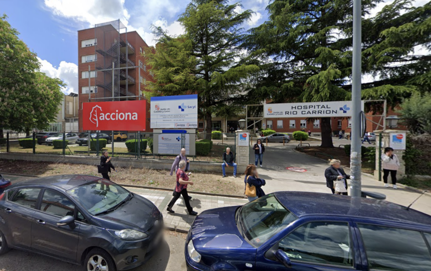 Carteles de la constructora y de la Junta explicando el proyecto en el acceso al Hospital Río Carrión con varios ciudadanos paseando delante de ellos.