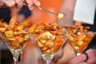 copa con patatas bravas sobre un fondo desenfocado donde se ve una mano con un tenedor