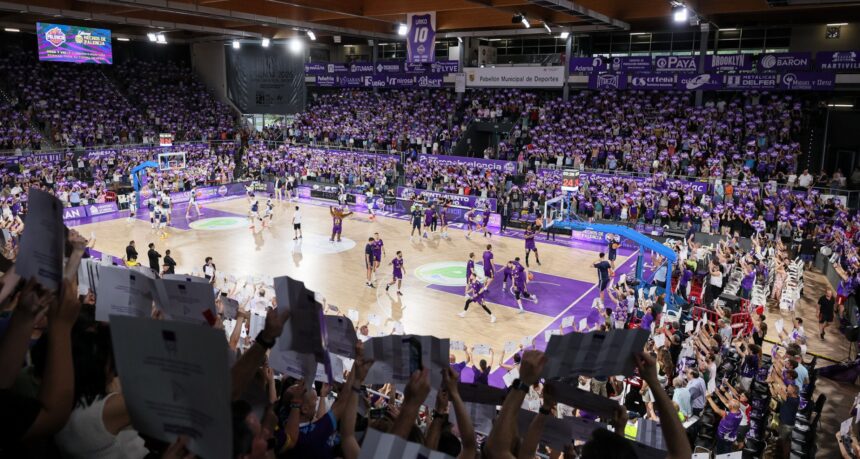 cientos de aficionados sostienen pancartas moradas mientras en la cancha los jugadores de baloncesto calientan