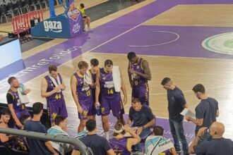 Varios jugadores de balocesto rodean al entrenador, sentado en una silla en la cancha de baloncesto