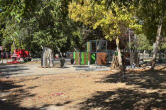 palets, tubos de aluminio y un elemento de juegos infantiles en un suelo de tierra y bajo unos árboles