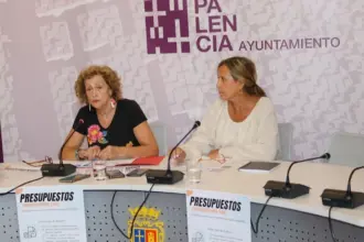 Dos muejres sentandas en un mesa delante de un cartelón promocional del Ayuntamiento de Palencia