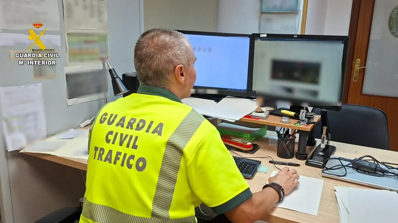 Un guardia civil de tráfico sentado delante de las pantallas del ordenador en una mesa de oficina.