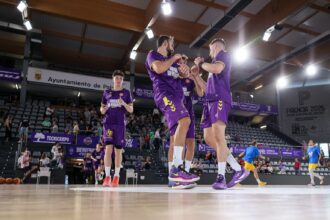 Varios jugadores del Palencia Baloncesto están en el centro de la pista durante el calentamiento chocando y divirtiéndose mientras al fondo hay jugadores del otro equipo.