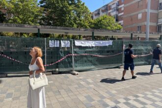 Ciudadanos caminan delante de las vallas de obra que delimitan los trabajos de reforma integral de la plaza Rabí Sem Tob.