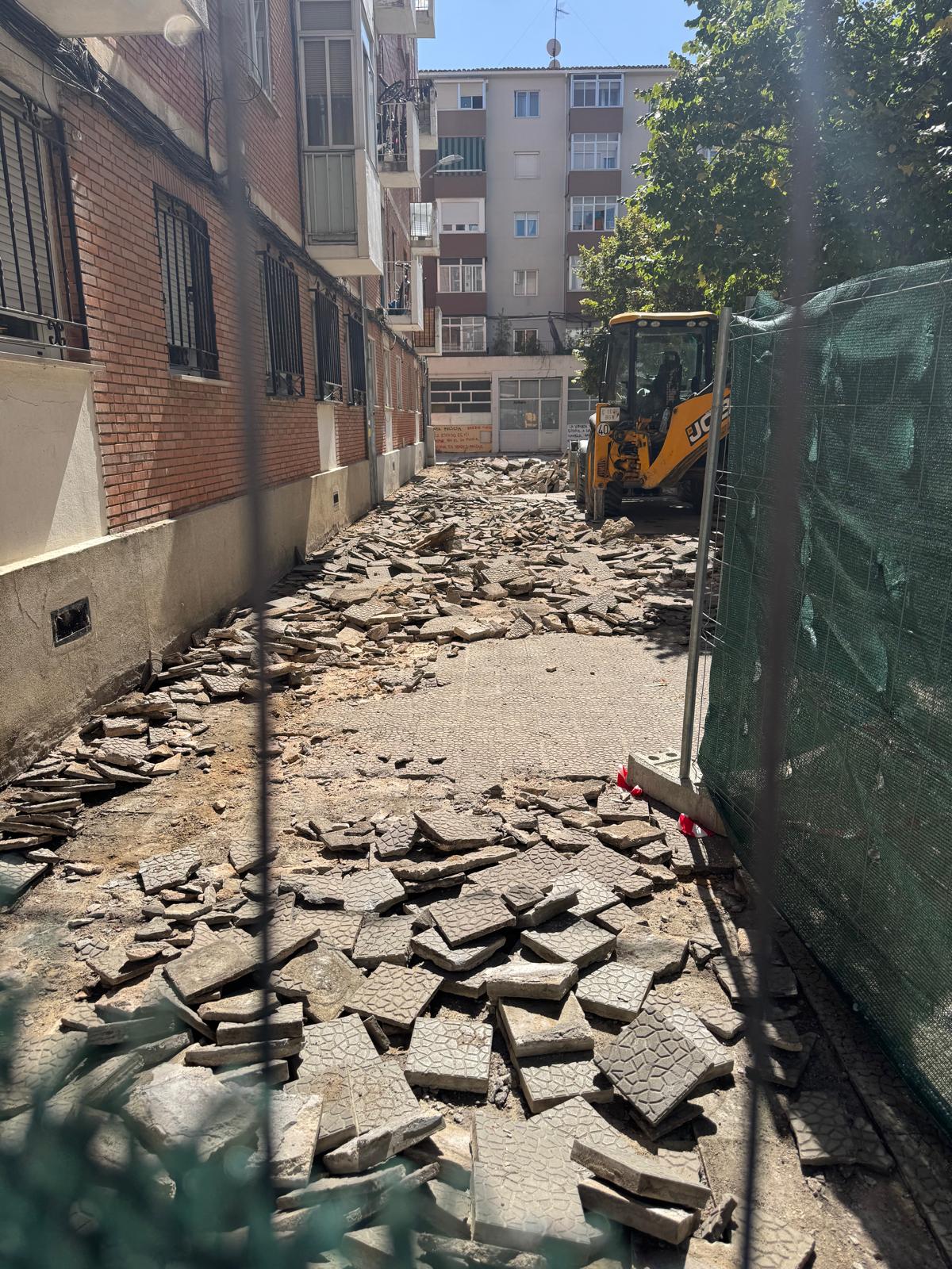 Baldosas picadas y levantadas con maquinaría de obra al fondo en uno de los accesos de la plaza Rabí Sem Tob.