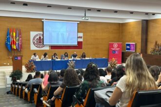 Alumnos sentados en un salón de actos escuchando a los vicerrectores que están ubicados en el escenario.