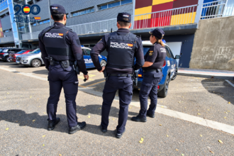 Tres Policías Nacionales de espaldas, junto a varios vehículos policiales.