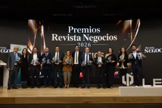 Varias personas posan con un galardón en la mano delante de una pantalla en la que se puede leer Premios Revista Negocios 2026.