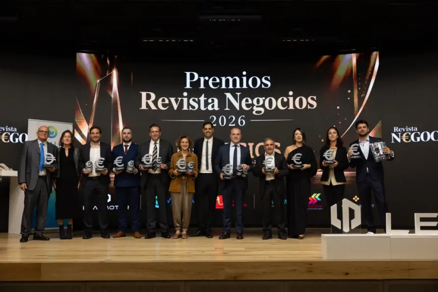 Varias personas posan con un galardón en la mano delante de una pantalla en la que se puede leer Premios Revista Negocios 2026.