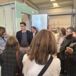 Varias personas escuchan lo que dice otra en la visita a una fábrica