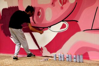 Un hombre pinta con un spray una obra de arte en un mural