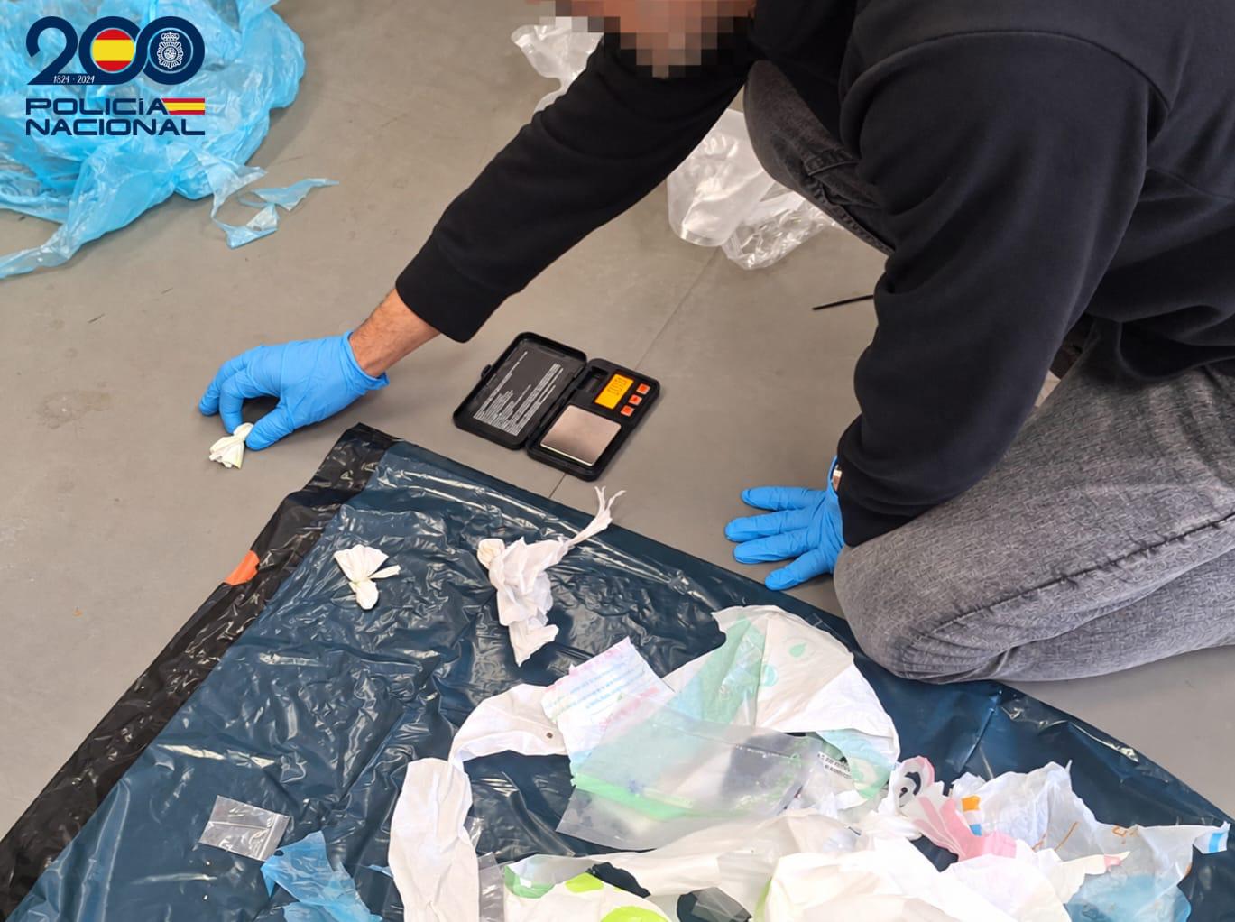 Policía sacando de una bolsa de basura localizada en un contenedor drogas y material para la preparación de dosis.