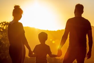 Un hombre y una mujer dan la mano a un niño a contraluz