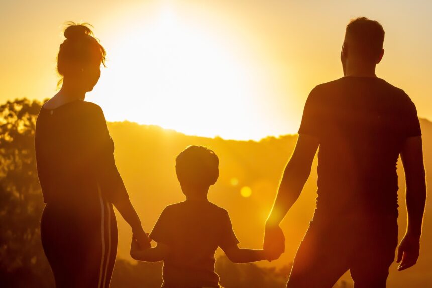 Un hombre y una mujer dan la mano a un niño a contraluz